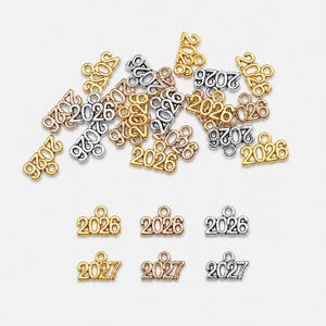 May include: A collection of metal charms shaped as the numbers 2026 and 2027, featuring gold, silver, and rose gold finishes. Each charm includes a small circular loop at the top for attachment, with the year clearly embossed on the front surface.