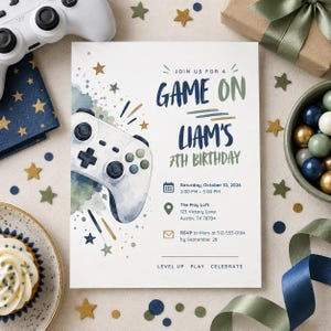 Könnte beinhalten: Eine rechteckige Geburtstagseinladungskarte mit einer Aquarellillustration eines weißen Gamecontrollers, goldenen Sternen sowie blauen und grünen Farbspritzern. Der Text lautet: JOIN US FOR A GAME ON LIAM'S 7TH BIRTHDAY, Saturday, October 10, 2026, 2:00 PM - 5:00 PM, The Play Loft, 123 Victory Lane, Austin, TX 78704, RSVP to Mom at 512-555-0184 by September 28, LEVEL UP PLAY CELEBRATE.