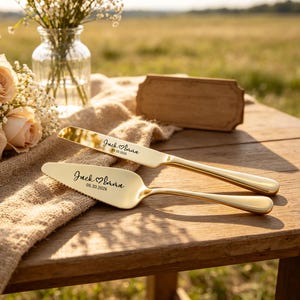 May include: A gold-toned cake knife and server set featuring a polished metallic finish. Both pieces are engraved with the text Jack ♡ Emma and the date 05.20.2026 in a black script font. The server has a serrated edge on one side.