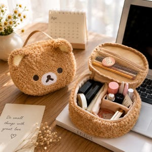 May include: A brown fuzzy bear-shaped cosmetic bag with a zippered closure. The interior features a mesh pocket in the lid and multiple compartments containing various small beauty items, including cylindrical containers and compacts.