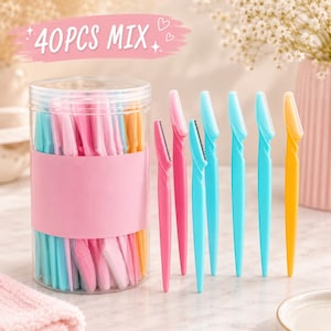 May include: A clear plastic cylindrical container filled with a 40PCS MIX of colorful eyebrow razors in shades of pink, blue, and yellow. Six individual razors in matching colors are arranged upright outside the container, each featuring a safety blade.