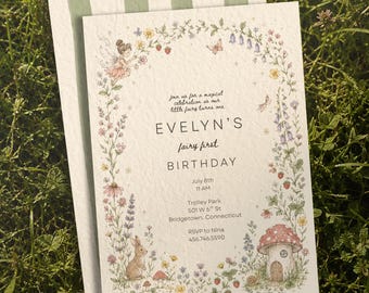 May include: A white rectangular birthday invitation card featuring a floral border with a fairy, a rabbit, and a mushroom house. The text reads: Join us for a magical celebration as our little fairy turns one, EVELYN'S fairy first BIRTHDAY, July 8th, 11 AM, Trolley Park, 501 W 6th St, Bridgetown, Connecticut, RSVP to Nina, 456.746.5590.