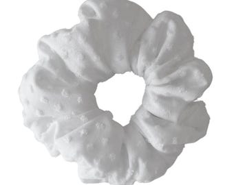 May include: A white scrunchie with a textured, dotted pattern. The hair accessory is made of soft fabric and is designed to hold hair in place. The scrunchie is a simple, yet stylish hair accessory.