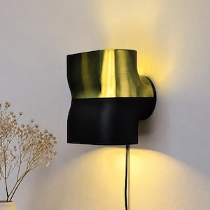Könnte beinhalten: Eine Wandleuchte in zylindrischer Form mit einem metallisch goldenen oberen Teil und einem mattschwarzen unteren Teil. Die Leuchte strahlt ein warmes, leuchtendes Licht aus den oberen und unteren Öffnungen aus und erzeugt einen sanften Schein.