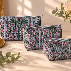 May include: A set of three rectangular quilted pouches in varying sizes, featuring a light blue background with a repeating dark green vine and pink floral pattern, finished with a black and white striped zipper trim along the top edge.