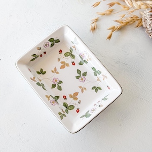 May include: A rectangular white ceramic tray featuring a delicate botanical pattern of small red strawberries, green leaves, and light pink flowers scattered across the interior surface, finished with a thin metallic rim.