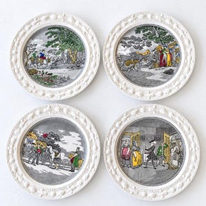 May include: A set of four round ceramic plates with cream-colored embossed rims featuring fruit and floral motifs. Each plate displays a detailed, multi-colored historical scene with figures, animals, and landscapes set against a gray background.