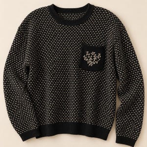 May include: A black long-sleeve sweater featuring a repeating white dotted pattern, a solid black crew neckline, cuffs, and hem, and a single black chest pocket adorned with a delicate, light-colored embroidered floral branch design.