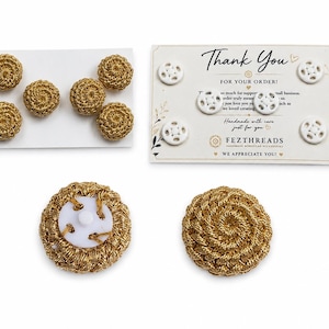 May include: A collection of round buttons featuring a metallic gold crocheted texture and a white plastic backing. The set includes several gold buttons on a white card and white buttons on a Thank You card with the text FEZTHREADS.