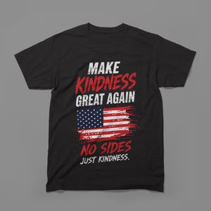 Puede incluir: Una camiseta negra de manga corta con un estampado gráfico que incluye el texto "MAKE KINDNESS GREAT AGAIN" en rojo y blanco, una ilustración de la bandera estadounidense desgastada y el texto "NO SIDES JUST KINDNESS" en letras rojas y blancas.