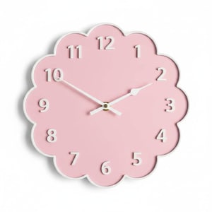 May include: A round wall clock with a scalloped edge, featuring a solid light pink face and a white border. The clock has raised white Arabic numerals from 1 to 12 and two thin white hands centered on the face, indicating the current time.