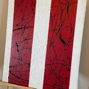 May include: A rectangular canvas painting featuring vertical stripes of solid red and textured white. The red sections are overlaid with thin, chaotic black paint splatters, while the white sections have a raised, thick, and uneven surface texture.