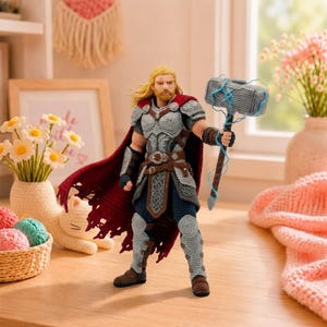 May include: A crocheted amigurumi figure of a warrior with long blonde hair and a beard, wearing grey armour, a dark red cape, and brown boots. The figure holds a large grey hammer with blue yarn lightning accents extending from the head to the handle.