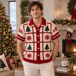 Pode incluir: Uma camisa de crochê de manga curta com botões, apresentando um padrão de grade na cor creme com motivos alternados de árvores de Natal e flocos de neve em vermelho e verde. A peça tem gola, punhos e bainha vermelhos com botões claros.