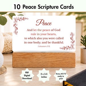 May include: A rectangular white card featuring the text Peace And let the peace of God rule in your hearts, to which also you were called in one body; and be thankful. Colossians 3:15 with red floral borders, displayed on a wooden stand.