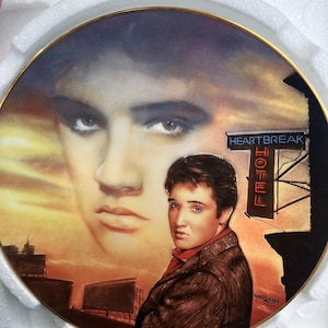 Puede incluir: Un plato decorativo de colección redondo que presenta un retrato de Elvis Presley con una imagen facial grande y desvanecida en el fondo y una figura más pequeña en primer plano. La escena incluye un letrero que dice Heartbreak Hotel y un cielo al atardecer.