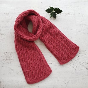May include: A pink knitted scarf with a cable knit pattern.