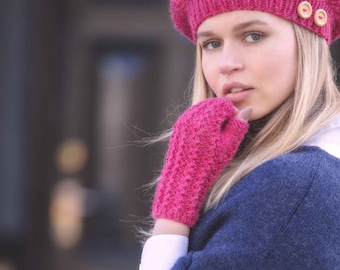 May include: A woman wearing a pink knitted beret with two buttons on top, a pink knitted fingerless glove, and a dark blue sweater.