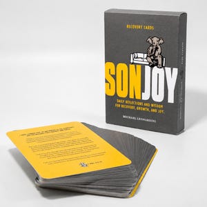 May include: A deck of recovery cards with a yellow top card featuring black text and an elephant illustration. Beside the deck stands a dark gray box labeled SONJOY with yellow and white text, an elephant graphic, and the author Michael Leonardini.