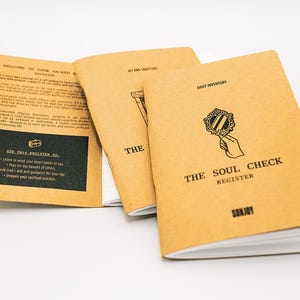 May include: Three tan paper journals with black ink text and illustrations. The front cover features a hand holding a mirror and the text THE SOUL CHECK REGISTER. The open interior page displays a black rectangular box with white text instructions.