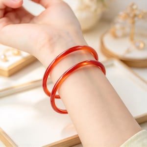 May include: Two smooth, translucent, deep orange-red circular bangles worn on the wrist. The bracelets feature a polished, glossy finish with a consistent rounded profile, showcasing a vibrant, uniform color throughout the solid material.