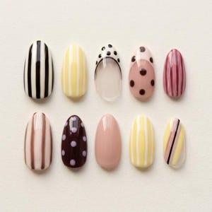 May include: A set of ten press-on nails in an almond shape, featuring various designs including black and white vertical stripes, yellow and white stripes, clear with black polka dots, pink with brown polka dots, mauve stripes, and solid light pink.