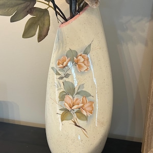 Peut inclure: Un grand vase en céramique en forme de goutte d'eau avec une base couleur crème parsemée de taches sombres. Le vase est orné d'un motif floral peint représentant des fleurs pêche douces et des feuilles vert sourd. Le bord a un accent rose.