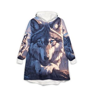 May include: A hooded sweatshirt featuring a large, detailed graphic of a wolf with piercing blue eyes. The design includes two additional wolf faces on the sleeves, set against a mountain landscape. The garment has a white hood and cuffs.