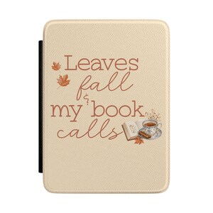 Puede incluir: Una funda para lector electrónico de color beige con el texto marrón Leaves fall & my book calls. El diseño incluye dos hojas de arce naranjas, un libro abierto, una taza de té sobre un platillo y una rama de canela sobre una superficie clara.