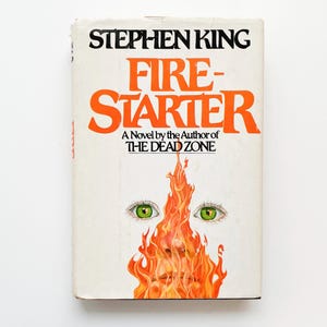 May include: A vintage paperback book titled "Firestarter" by Stephen King. The cover features orange flames, green eyes, and the text "A Novel by the Author of The Dead Zone."