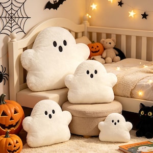 May include: Four white plush ghost-shaped cushions with embroidered black eyes and open mouths. The cushions vary in size, featuring a soft, fuzzy texture. Each ghost has a rounded head and two small arms extending from the sides of the body.