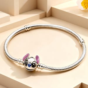 Peut inclure: Un bracelet en chaîne serpent argentée avec un charm représentant le personnage Stitch. Le charm présente de grands yeux noirs, un nez bleu foncé et des oreilles intérieures roses. Le bracelet comporte deux stations argentées fixes.