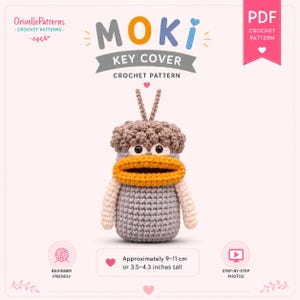 May include: A crochet pattern for a Moki key cover, featuring a light gray creature with a textured brown cap, two antennae, and a wide orange mouth. The PDF document includes text, beginner-friendly icons, and states a height of 3.5–4.3 inches.