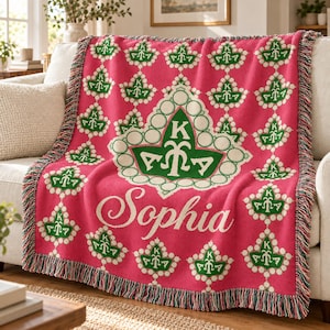 May include: A woven throw blanket in bright pink featuring a repeating pattern of green ivy leaf symbols with the letters AKA. A large central ivy emblem displays the letters AKA, and the name Sophia is written in white script below it.
