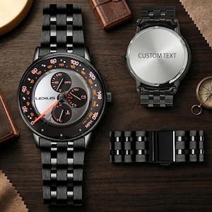 May include: A black metal wristwatch with a silver dial featuring the Lexus logo, orange numerical markers, and three sub-dials. The watch includes a matching black link bracelet and a separate case back with the text CUSTOM TEXT engraved on it.