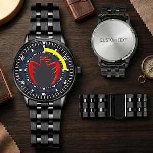 Pode incluir: Um relógio de pulso de metal preto com pulseira de elos, apresentando um mostrador escuro com um gráfico de águia vermelha, um arco amarelo e marcadores brancos. O verso do relógio mostra o texto CUSTOM TEXT e um segmento de pulseira é incluído.