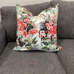 May include: A white pillow with a floral pattern in shades of pink, green, and black. The pillow is on a gray couch.
