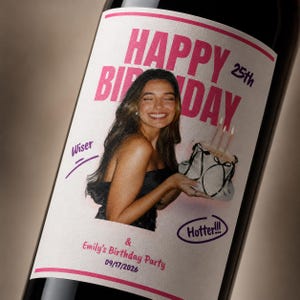 May include: A wine bottle label featuring a photo of a smiling person holding a cake with candles. The text reads HAPPY 25th BIRTHDAY, Wiser, Hotter!!!, and Emily's Birthday Party 09/17/2026. The design uses pink and purple accents on a white background.