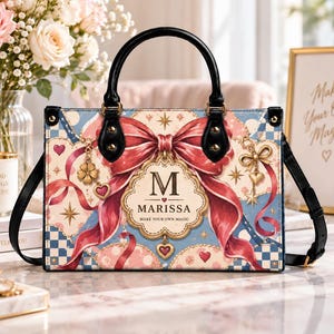 Könnte beinhalten: Eine rechteckige Handtasche mit schwarzen Griffen und einem Schulterriemen. Die Tasche zeigt ein hellblaues und cremefarbenes Karomuster, eine große rote Schleife und ein zentrales Emblem mit dem Buchstaben M, dem Namen Marissa und dem Text Make Your Own Magic.
