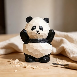 Op de afbeelding: Een handgesneden houten pandabeeldje met een gefacetteerde oppervlaktestructuur. De beer is beschilderd met een wit gezicht, borst en buik, gecontrasteerd door zwarte oren, oogvlekken, armen en benen. Het figuur staat rechtop met een ronde vorm.