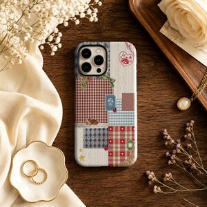 May include: A smartphone case featuring a patchwork design of red and white gingham, blue and white checkered patterns, cream cable knit textures, and small illustrations of hearts, stars, ladybugs, and a small deer on a white background.