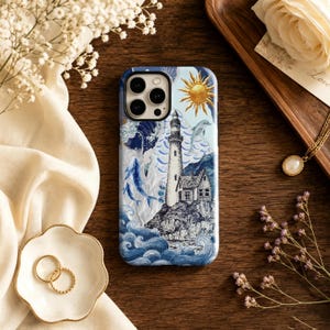 May include: A smartphone case featuring a detailed illustration of a lighthouse on a rocky shore, surrounded by blue ocean waves, a golden sun, a dolphin, and whales. The design incorporates intricate line work and shades of blue and white.