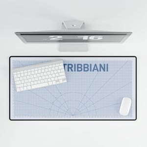 May include: A rectangular desk mat featuring a blue grid pattern with circular markings and the text TRIBBIANI in blue. The mat is positioned under a white wireless keyboard and a white computer mouse, with a computer monitor visible above.