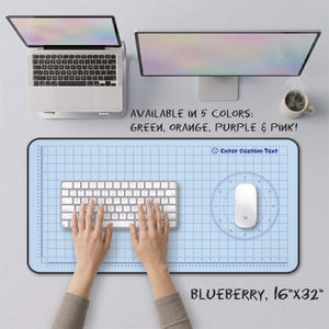 May include: A light blue rectangular desk mat featuring a dark blue grid pattern, a circular protractor design, and the text Enter Custom Text. The mat measures 16 inches by 32 inches. Text states it is available in green, orange, purple, and pink.