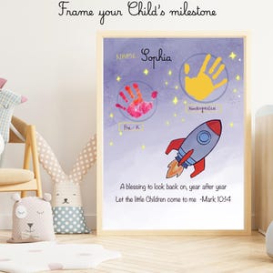 May include: A framed personalized milestone poster featuring a purple space-themed background with a rocket ship, yellow stars, and two handprints labeled Pre-K and Kindergarten. The text reads Name: Sophia and A blessing to look back on, year after year. Let the little Children come to me -Mark 10:14.