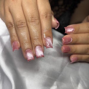 May include: A set of fingernails featuring a cat-eye polish effect in a shimmering dusty rose pink hue. The nails are shaped with a square tip, displaying a reflective, metallic-like streak that runs diagonally across the center of each nail surface.