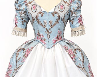 May include: A light blue dress featuring a floral pattern with pink roses and brown scrollwork. The bodice has a V-neckline and puff sleeves with cream-colored lace trim and hanging pearl-like beads. The skirt is white with a blue floral overlay.