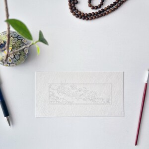 May include: A rectangular piece of white textured paper featuring a faint, intricate line drawing of a landscape within a thin border. The paper is positioned between a blue mechanical pencil on the left and a thin red paintbrush on the right.