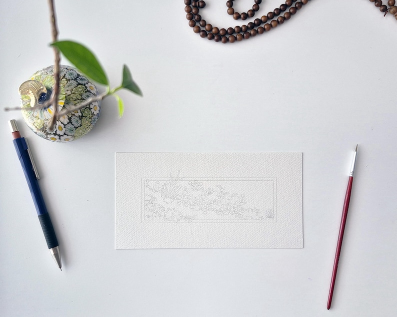 May include: A rectangular piece of white textured paper featuring a faint, intricate line drawing of a landscape within a thin border. The paper is positioned between a blue mechanical pencil on the left and a thin red paintbrush on the right.