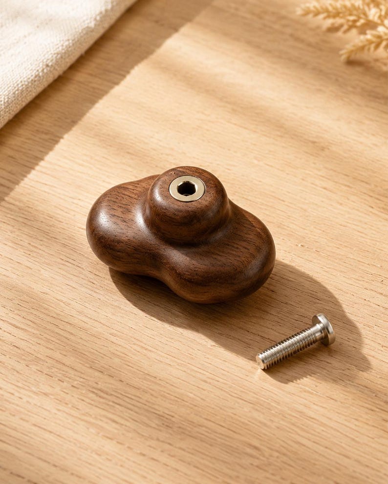 Peut inclure: Un bouton de meuble en bois brun fonc&eacute; avec une forme arrondie irr&eacute;guli&egrave;re et une finition lisse. Le centre pr&eacute;sente un insert m&eacute;tallique circulaire avec une ouverture hexagonale. Un boulon m&eacute;tallique argent&eacute; &agrave; t&ecirc;te plate est pos&eacute; &agrave; c&ocirc;t&eacute;.
